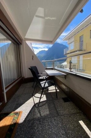 Un balcon avec une table et des chaises, une vue sur les montagnes et un bâtiment en arrière-plan.