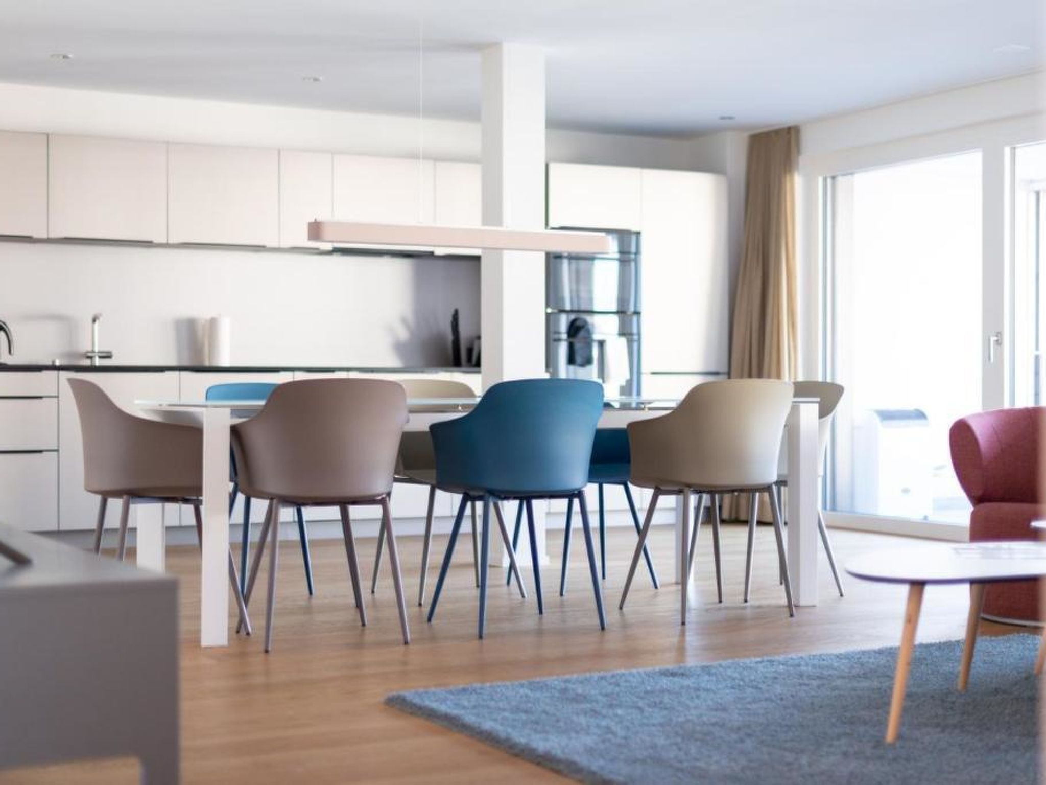 Una cocina moderna con armarios blancos, un comedor con cuatro sillas y un amplio ventanal con cortinas.