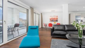 Una sala de estar moderna con un sillón azul, un sofá negro y un comedor con sillas rojas.