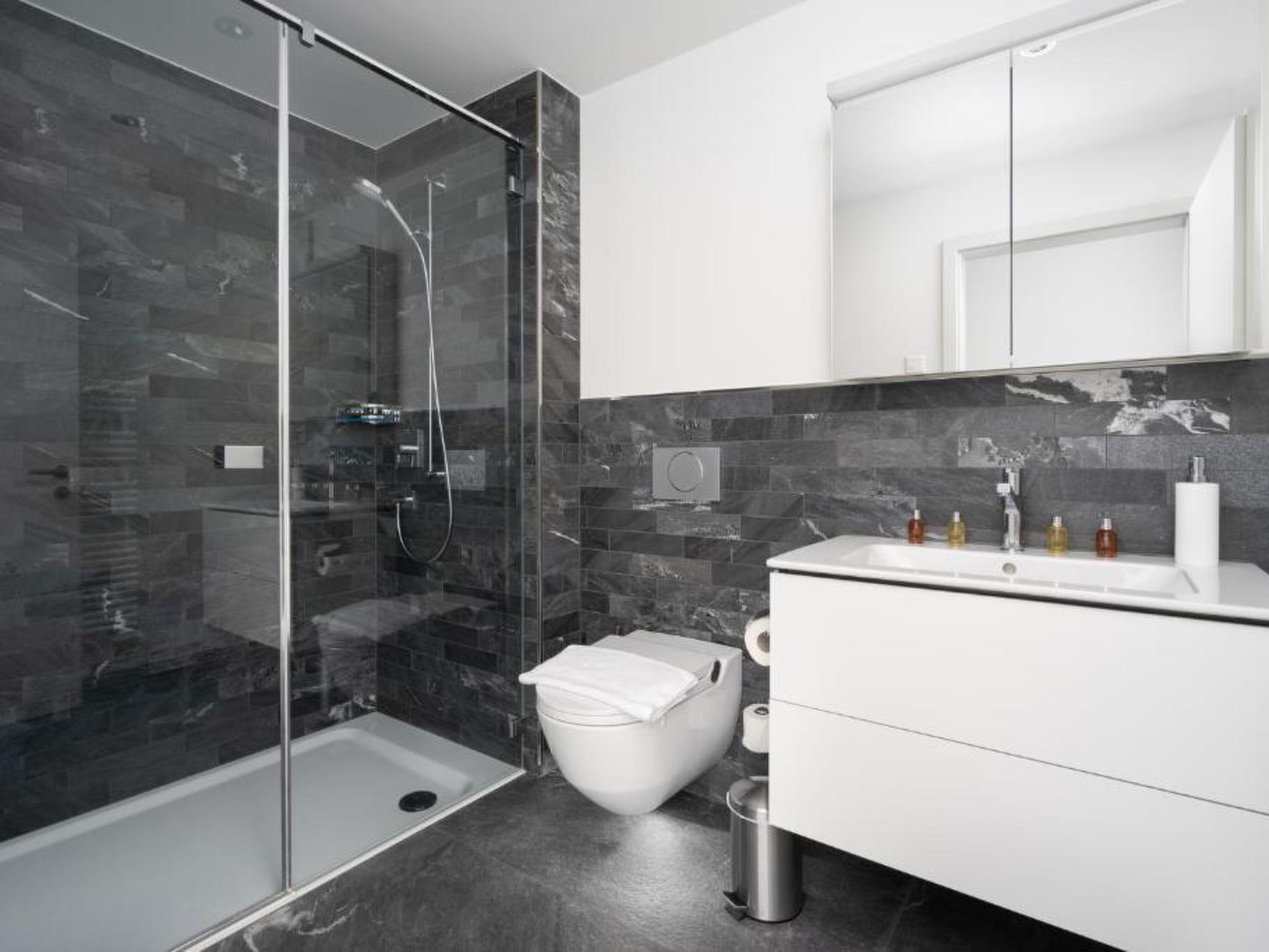 Un baño moderno con ducha envuelta en vidrio, inodoro blanco y tocador con espejo.