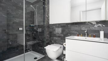 Un baño moderno con ducha envuelta en vidrio, inodoro blanco y tocador con espejo.