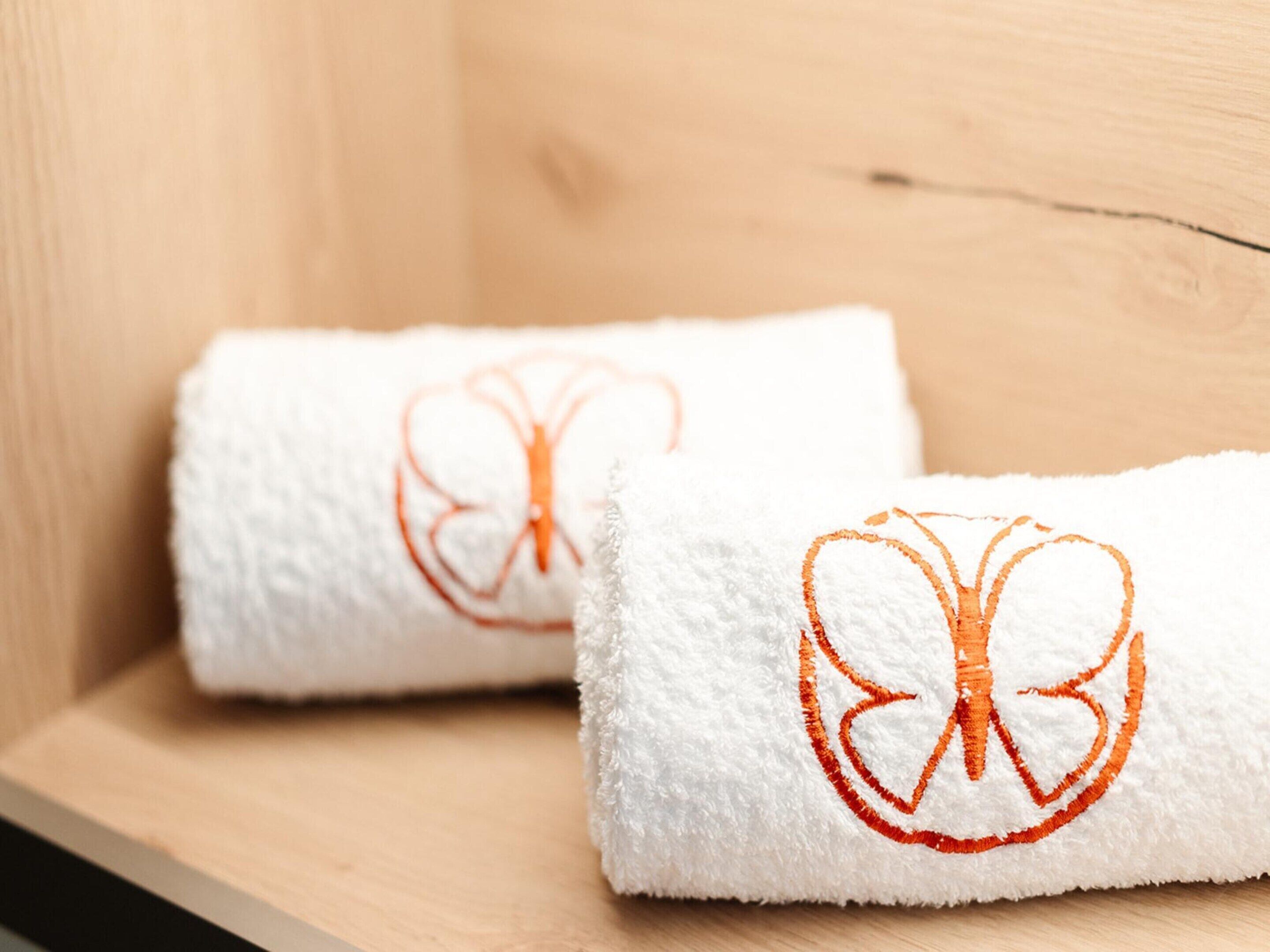 Two white towels with orange embroidery on a wooden surface.