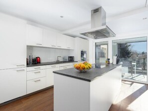 A modern kitchen with white cabinets, a central island with fruit, and a view through the glass door. - Swiss Hotel Apartments Appartement/Fewo Two Bedroom Apartment Kind & Twin by Interhome (Interlaken)