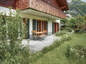 A wooden building with a covered patio, a table with chairs, and a garden with various plants and flowers. - CityChalet Appartement/Fewo Silberdistel**** by Interhome (Interlaken)