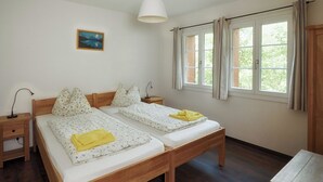 Et værelse med to træsenge, et natbord med lampe, et vindue med gardiner og et billede på væggen.
