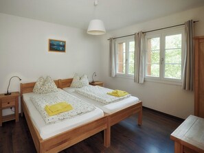 A room with two wooden beds, a bedside table with a lamp, a window with curtains, and a painting on the wall. - CityChalet Appartement/Fewo Silberdistel**** by Interhome (Interlaken)