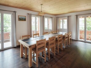 Un espace repas avec une longue table et des chaises en bois, de grandes fenêtres avec des rideaux et un plafond en bois.