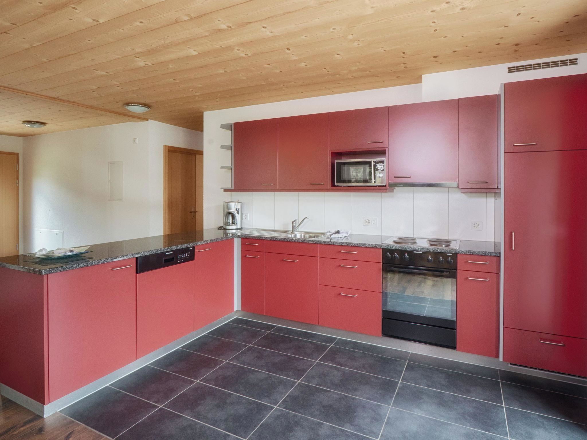 Eine moderne Küche mit roten Schränken, einer eingebauten Mikrowelle und einem Edelstahlbackofen.