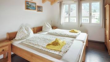 Una stanza con due letti di legno, un comodino, una finestra con tende e un soffitto in legno.