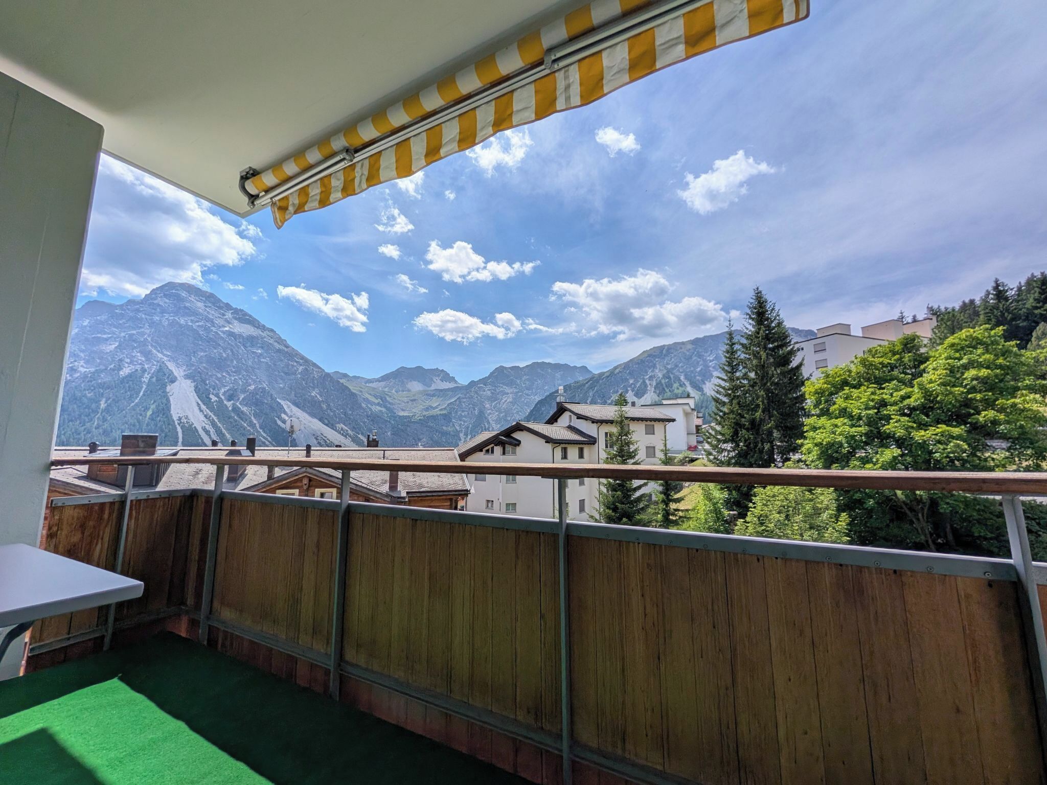 A balcony with a view of mountains, a wooden fence, and a table with a green mat.