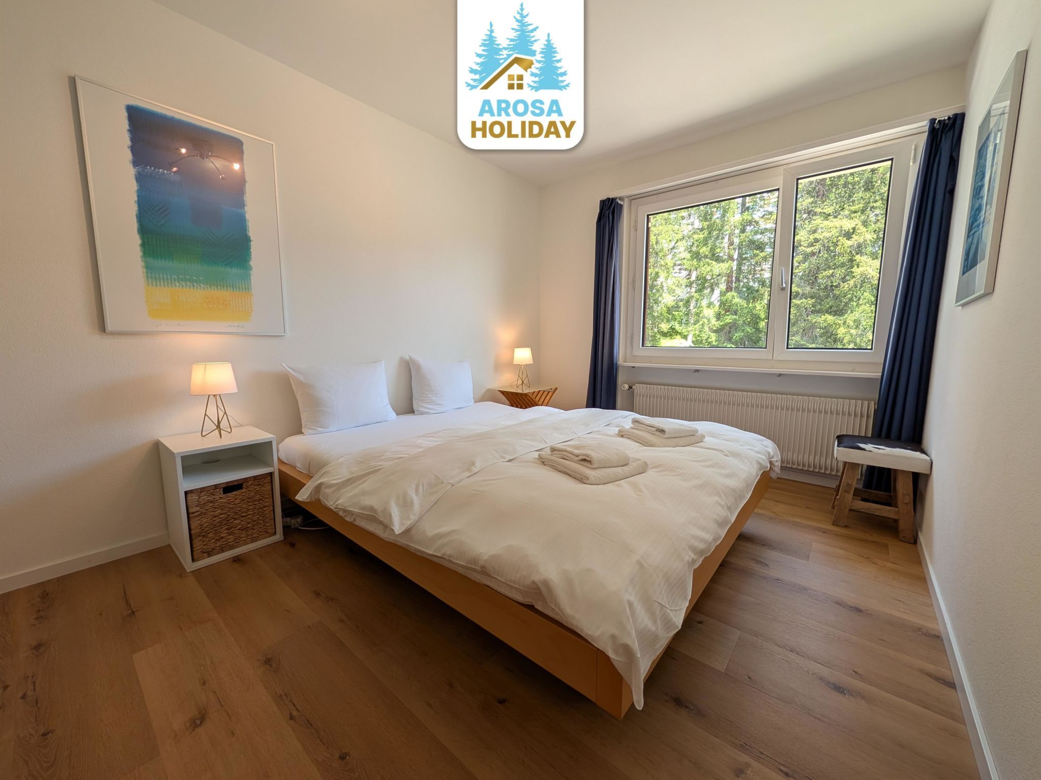 A bedroom with a bed, bedside table, lamp, and a window with curtains.