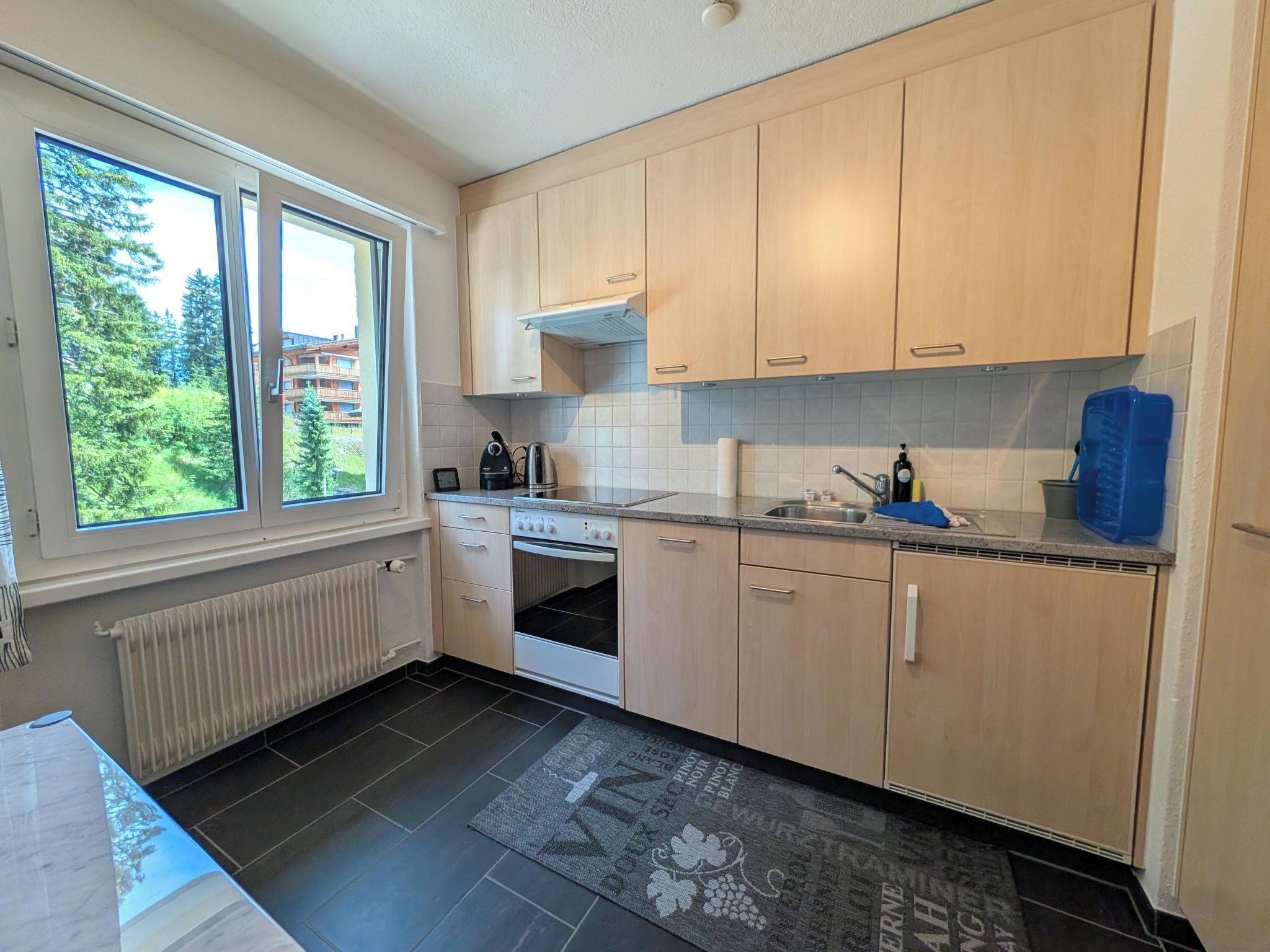A modern kitchen with wooden cabinets, a built-in oven, and a window overlooking a green landscape.