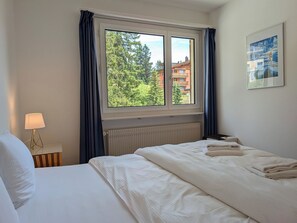 A hotel room with a bed, a window with curtains, a radiator, a lamp, and a painting on the wall. - Sunnaboda 1 by Arosa Holiday Appartement/Fewo, Dusche oder Bad, WC, 4-Bettwohnun by Interhome (Arosa)