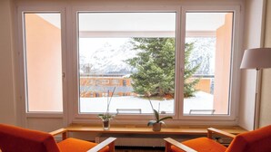 A room with a large window, two orange chairs, a small table, and a radiator. - Utoring Hohe Promenade 404 Appartement/Fewo, Dusche und Badewanne, 1 Schlafraum by Interhome (Arosa)