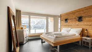 A bedroom with a wooden headboard, a bed with white linens, a nightstand with a lamp, and a view of snow-covered mountains through large windows. - Utoring Hohe Promenade 404 Appartement/Fewo, Dusche und Badewanne, 1 Schlafraum by Interhome (Arosa)