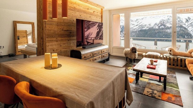 A cozy living room with a wooden wall, a TV, a dining table with chairs, a sofa, and a view of mountains. - Utoring Hohe Promenade 404 Appartement/Fewo, Dusche und Badewanne, 1 Schlafraum by Interhome (Arosa)