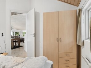 Une chambre à coucher avec un lit, une armoire en bois et un coin repas visible à travers une porte ouverte.