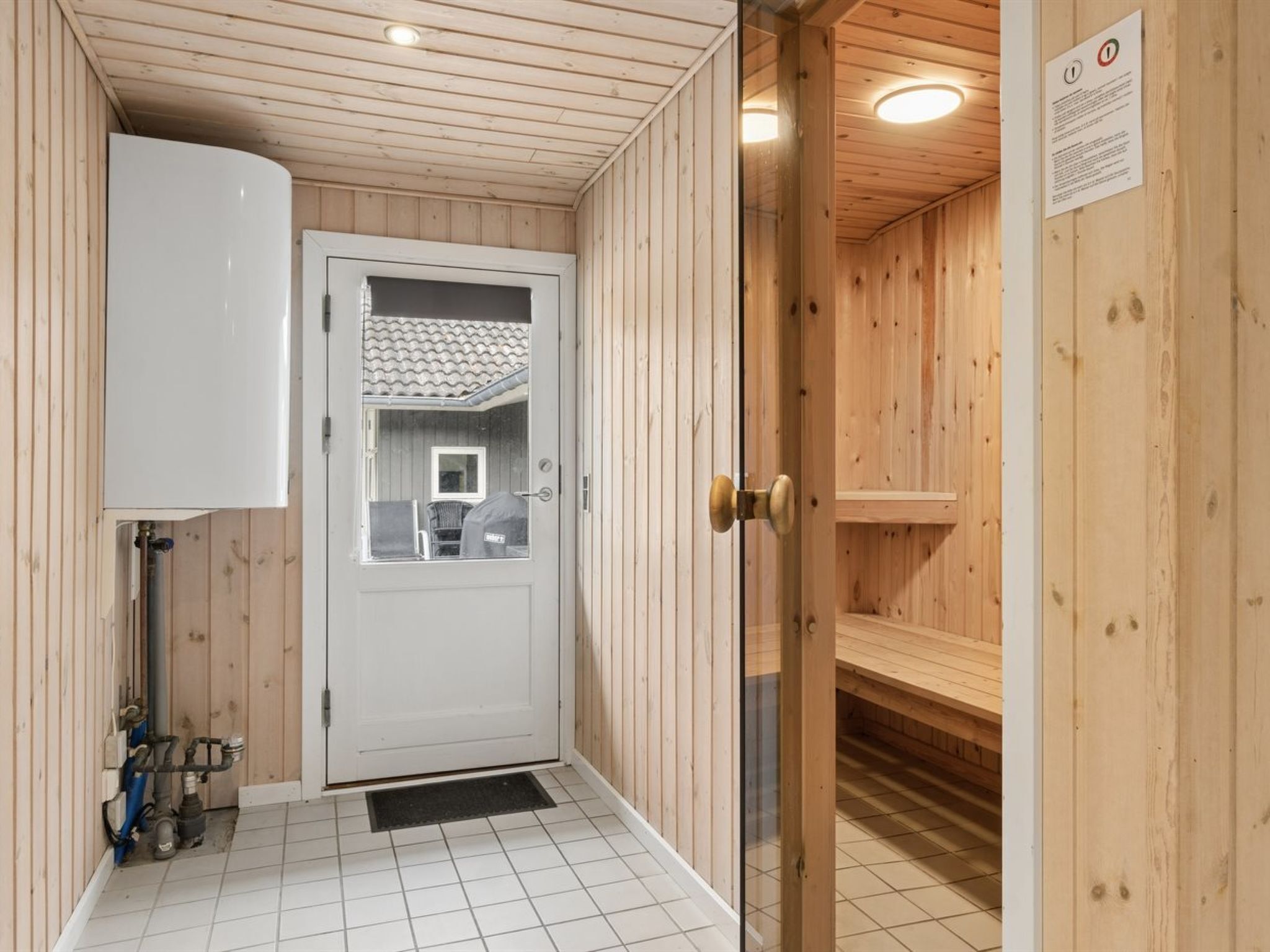Un sauna con paredes de madera, suelo de baldosas y una puerta que da a un baño con inodoro y lavamanos.