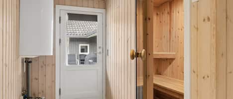 A sauna room with wooden walls, a tiled floor, and a door leading to a bathroom with a toilet and a sink.