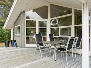 Ein überdachter Außenbereich mit Tisch und Stühlen, großen Fenstern und einer Holzterrasse.
