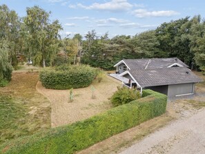 Ein eingeschossiges Haus mit geneigtem Dach, umgeben von einem gepflegten Garten und einer Schotterauffahrt.