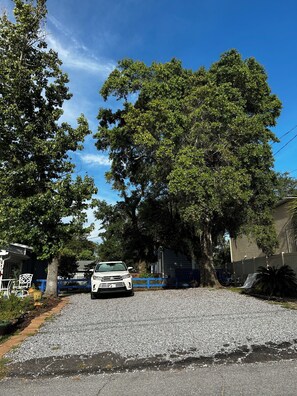 A white car parked on a gravel driveway with trees and a blue fence in the background. - Coastal Retreat Charming and Salty in St. Andrews/Panama City Florida (Panama City)