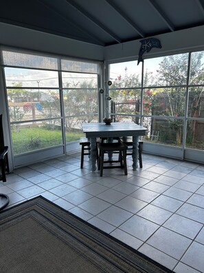 Ein Wintergarten mit Tisch und Stühlen, großen Fenstern und Blick ins Freie.