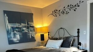 A bedroom with a bed, bedside tables, a lamp, a wall art piece, and a floor lamp. - Coastal Retreat Charming and Salty in St. Andrews/Panama City Florida (Panama City)