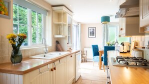 Una cocina con una isla central, un comedor con sillas azules y vistas al exterior.