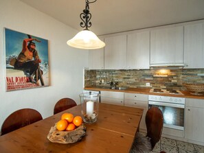 Eine Küche mit weißen Schränken, einer Küchenrückwand aus Stein und einem Holzespeisetisch mit einer Schüssel Orangen.