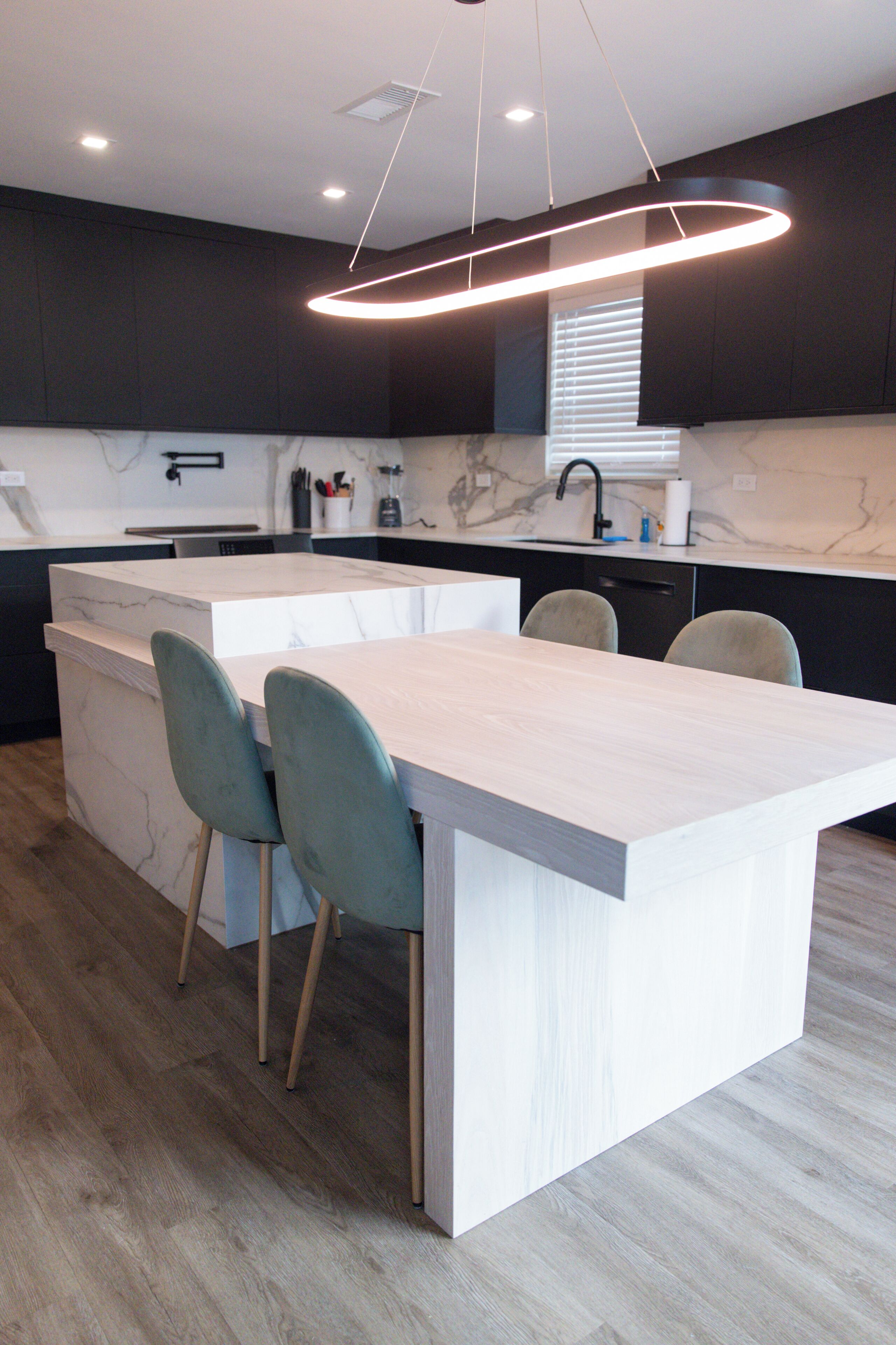 A modern kitchen with a central island, bar stools, and a pendant light.