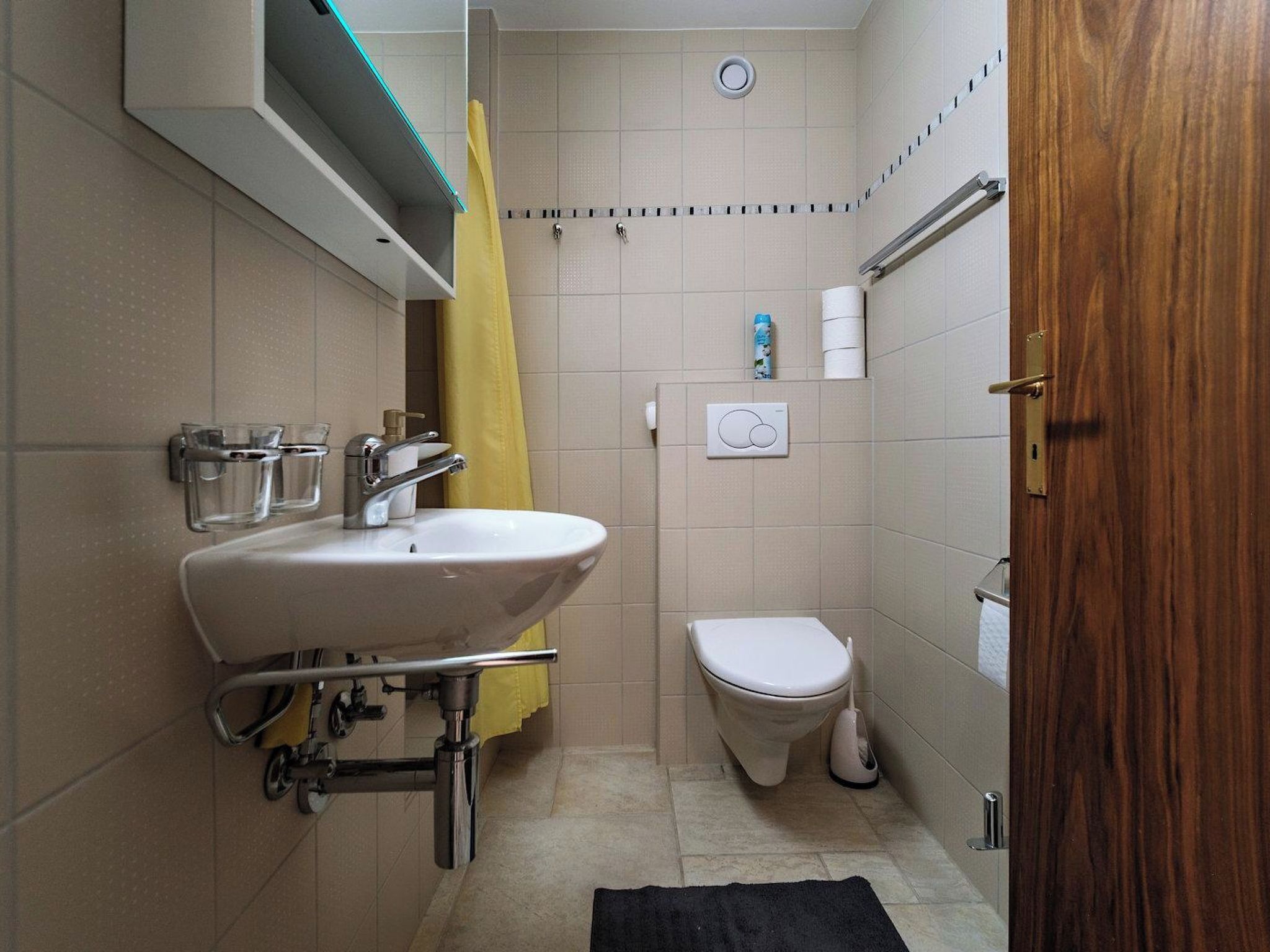 Ein Badezimmer mit Waschbecken, Toilette, Dusche und einer Holztür.