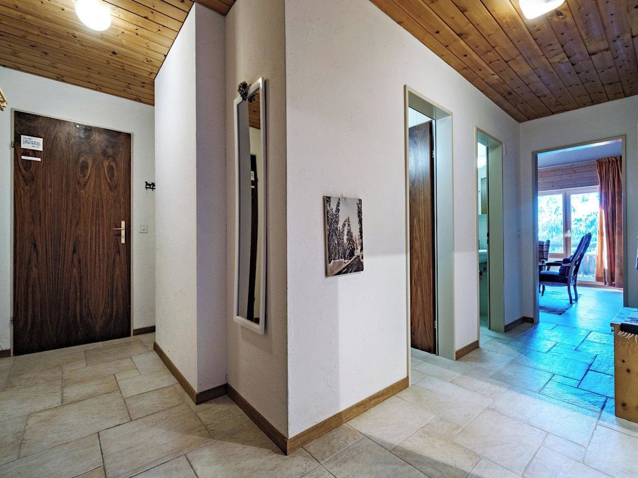 Um corredor com teto de madeira, uma porta com um aviso, um espelho e um quadro na parede.