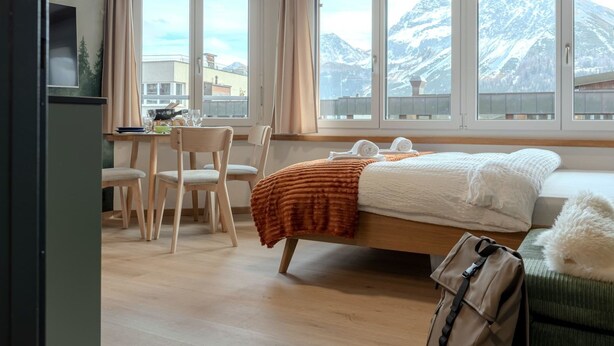 Ein Schlafzimmer mit einem Bett, einem Schreibtisch, Stühlen und Blick auf die Berge.
