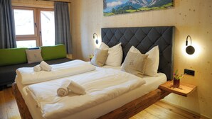 A double bed with white linens, a green sofa, wooden flooring, a painting of mountains, and a nightstand with a vase. - Benedikt – a cozy apartment steeped in history, perfect for unforgettable getaways (Gröbming)
