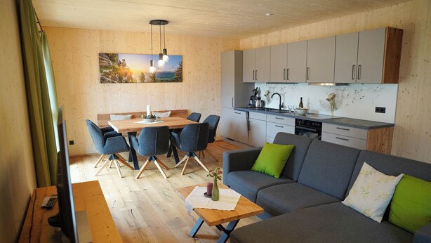 A modern living room with a grey sofa, a dining table with chairs, and a kitchen area with cabinets and a countertop. - Benedikt – a cozy apartment steeped in history, perfect for unforgettable getaways (Gröbming)
