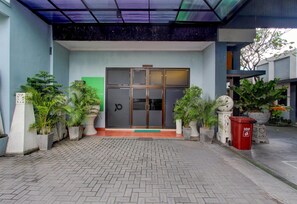 A hotel entrance with a glass door, potted plants, and a red trash bin. - Stylish Stay Near Malioboro (Yogyakarta)