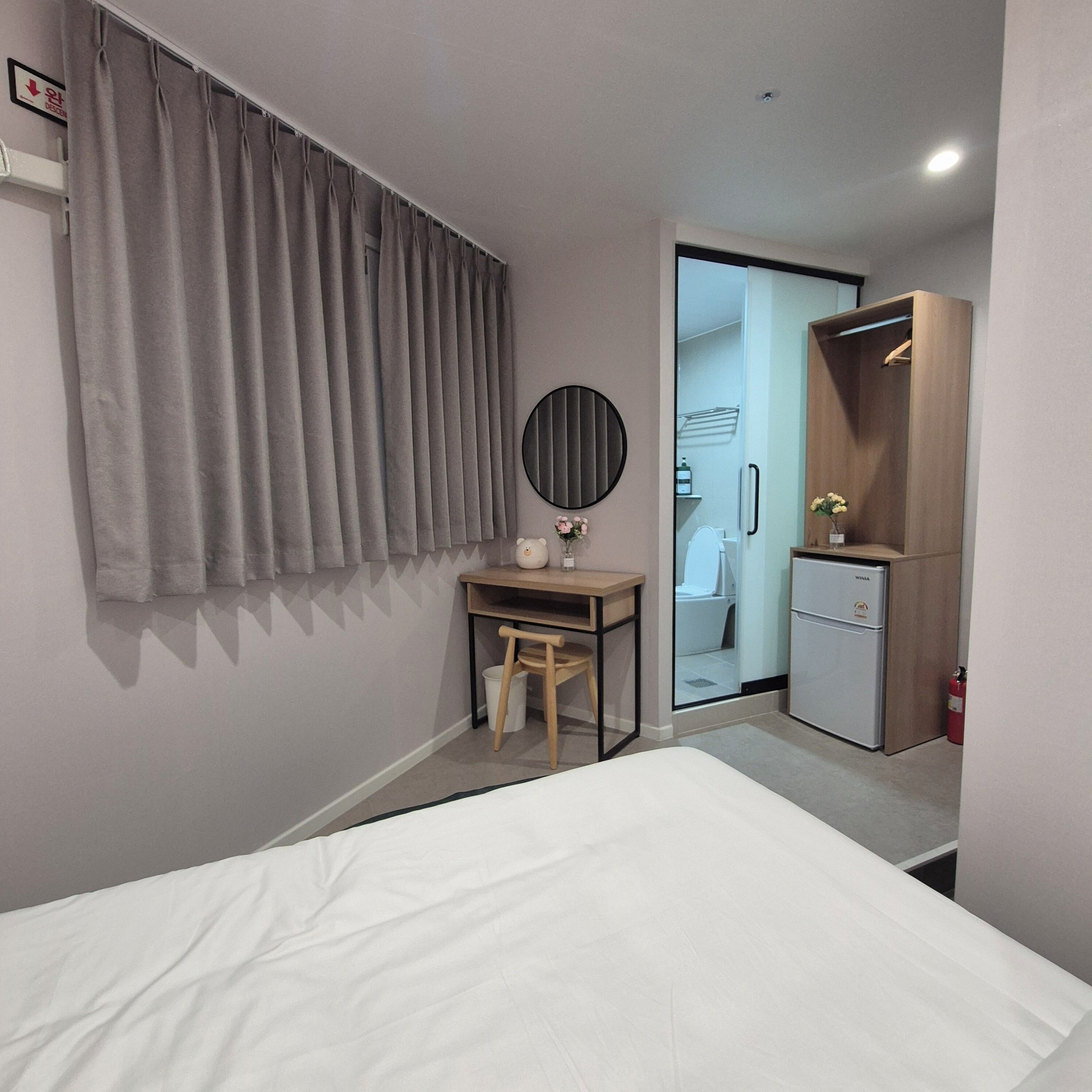A bedroom with a bed, a desk, a wardrobe, and a bathroom visible through a glass door.