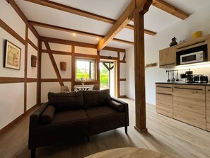 Ein Zimmer mit Holzbalken an der Decke, einer Couch, einem Esstisch mit Stühlen und einer Küchenzeile mit Holdekor und einer Mikrowelle.