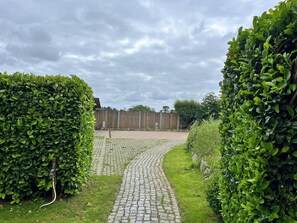 Un chemin pavé mène à une clôture en bois, qui est elle-même entourée de haies bien entretenues.