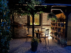An outdoor patio with a brick wall, wooden chairs, a table, and potted plants. - Neues Appartement mit Terrasse im Ferienhof Neuendorf (Luetow)
