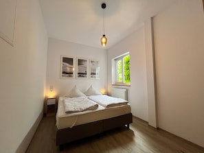 A bedroom with a bed, a window with a view of greenery, and three framed pictures on the wall. - Neues Appartement mit Terrasse im Ferienhof Neuendorf (Luetow)