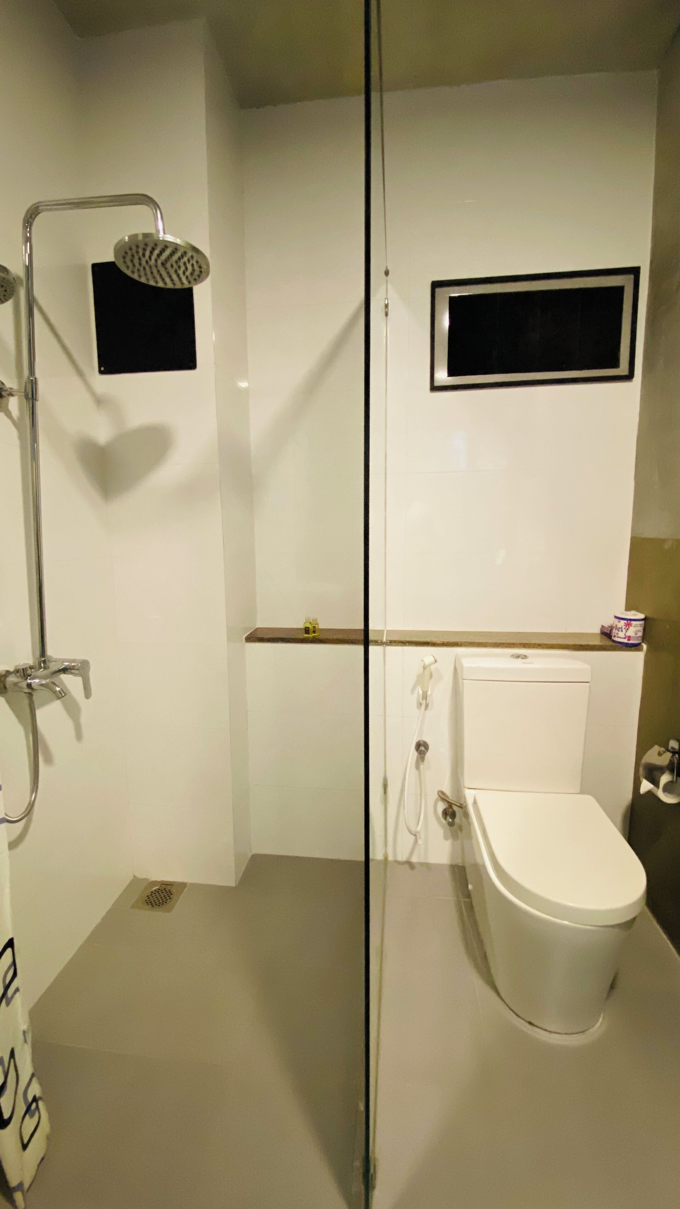 A bathroom with a shower, toilet, and a small window.