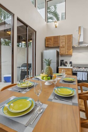 Een eethoek met een tafel voor vier personen, een koelkast en een keuken met houten kastjes.
