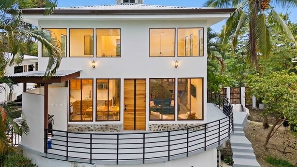 Una casa moderna de dos pisos con amplios ventanales, un balcón y una escalera que conduce al nivel superior.