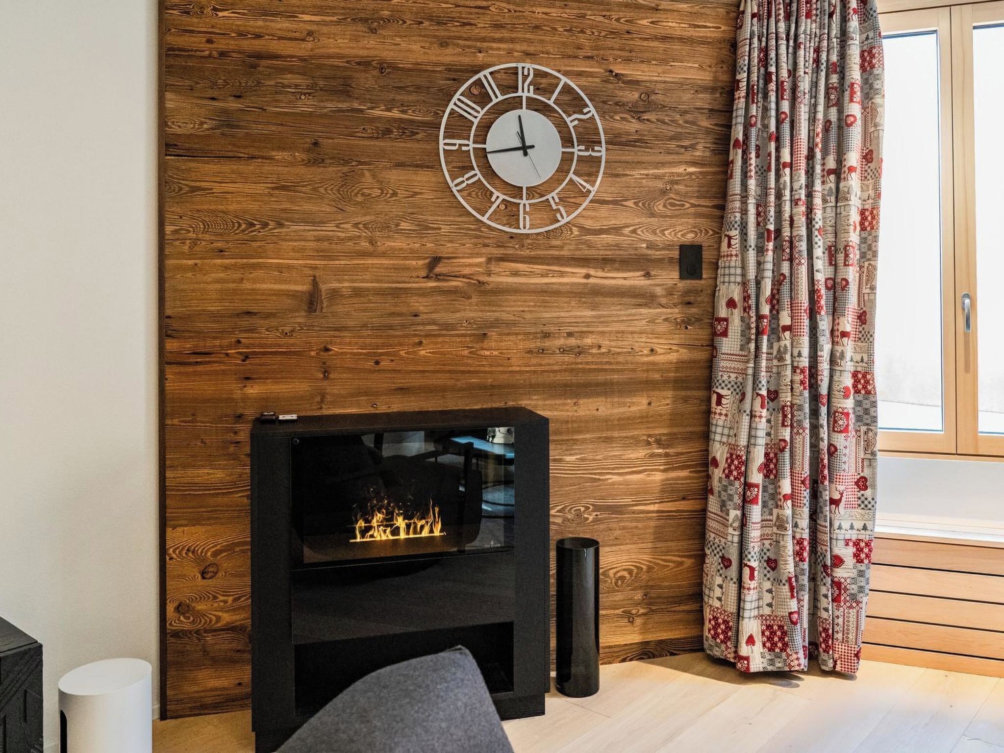 Ein Zimmer mit einer Holzwand, einem Kamin und einem gemusterten Vorhang.