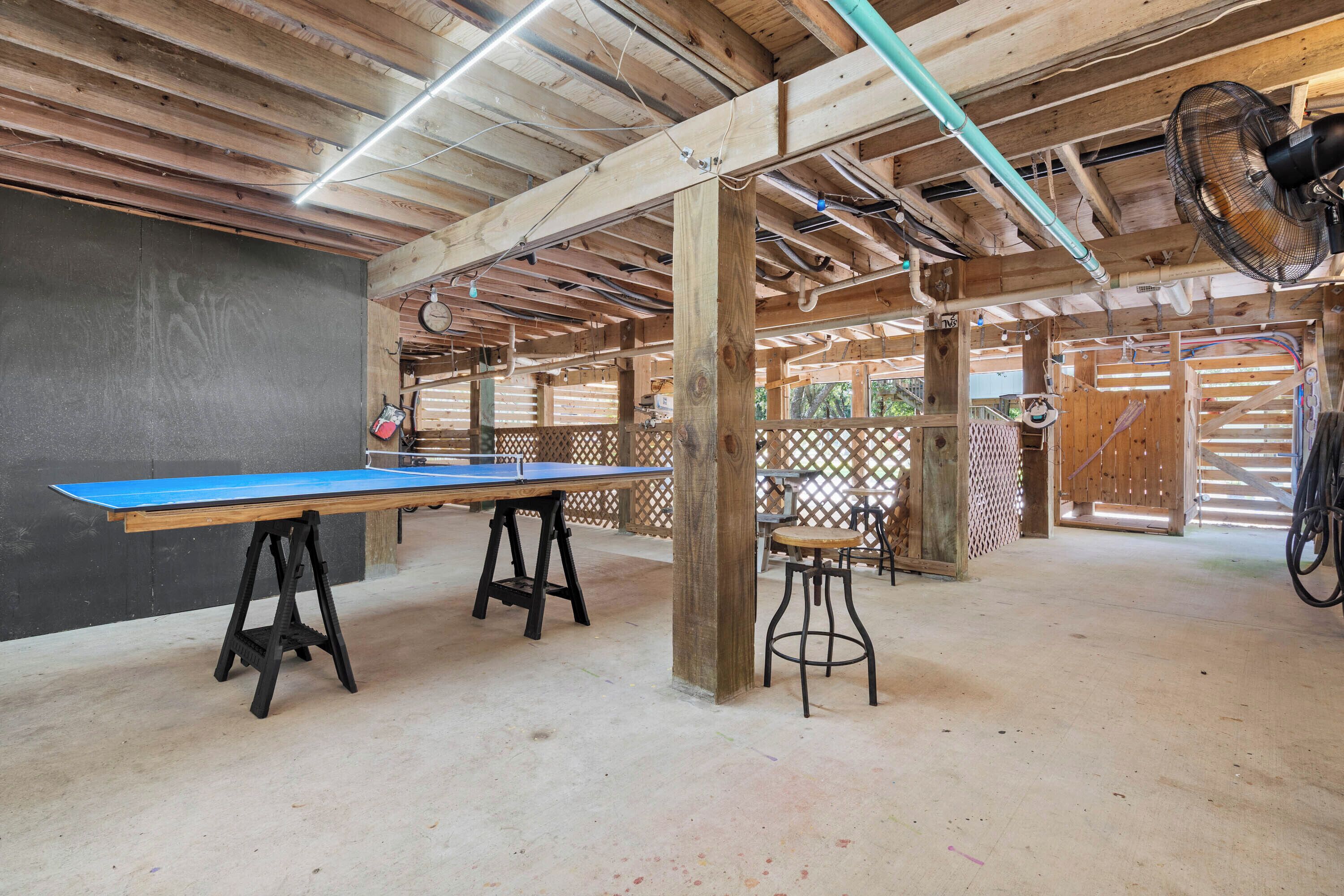 A ping pong table, stools, and a fan in a wooden room with a high ceiling.