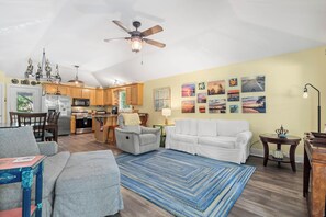 A spacious living area with a kitchen, a ceiling fan, and a dining table. - Wooded area home with private pool, pool table, and outdoor amenities (Dauphin Island)