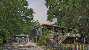 A two-story building with a porch and a staircase leading to the upper level. - Wooded area home with private pool, pool table, and outdoor amenities (Dauphin Island)
