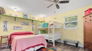 A room with a bunk bed, a desk, a chair, a shelf with pictures, and a window with blinds. - Wooded area home with private pool, pool table, and outdoor amenities (Dauphin Island)